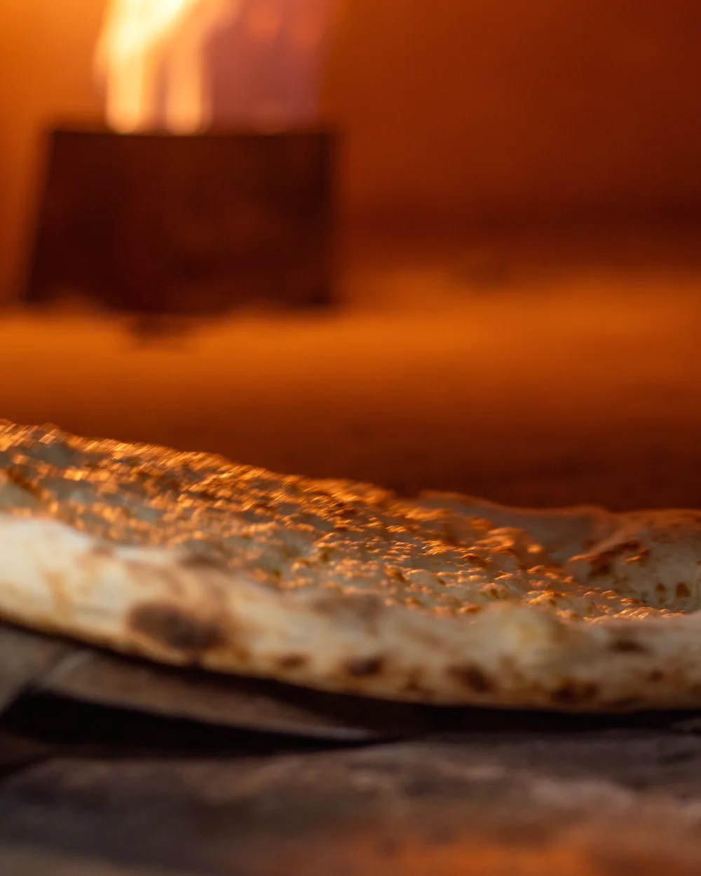 Pizza in cottura nel forno a legna, con la fiamma alta sul lato del forno