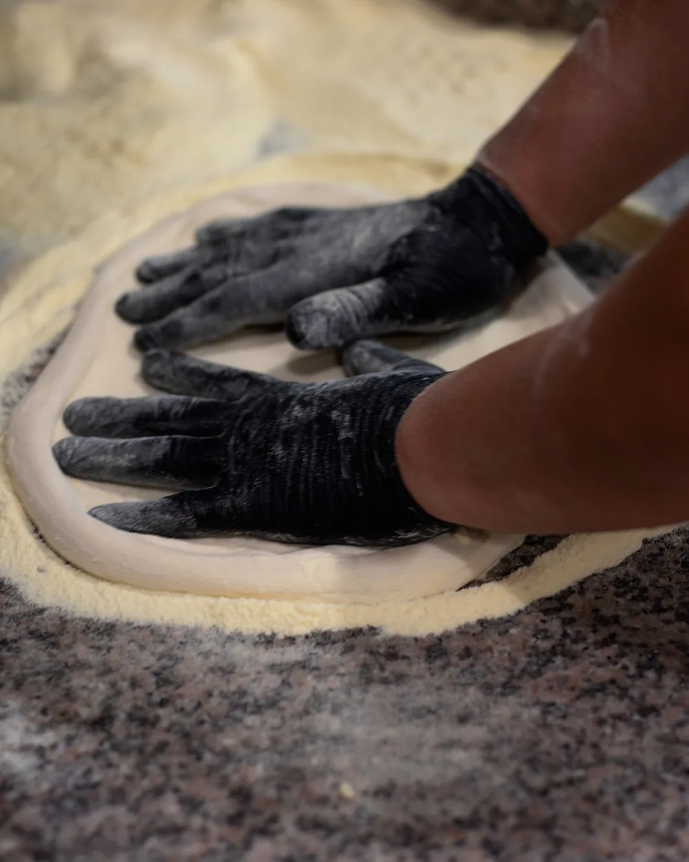 Le mani del pizzaiolo che stendono l'impasto sul marmo infarinato